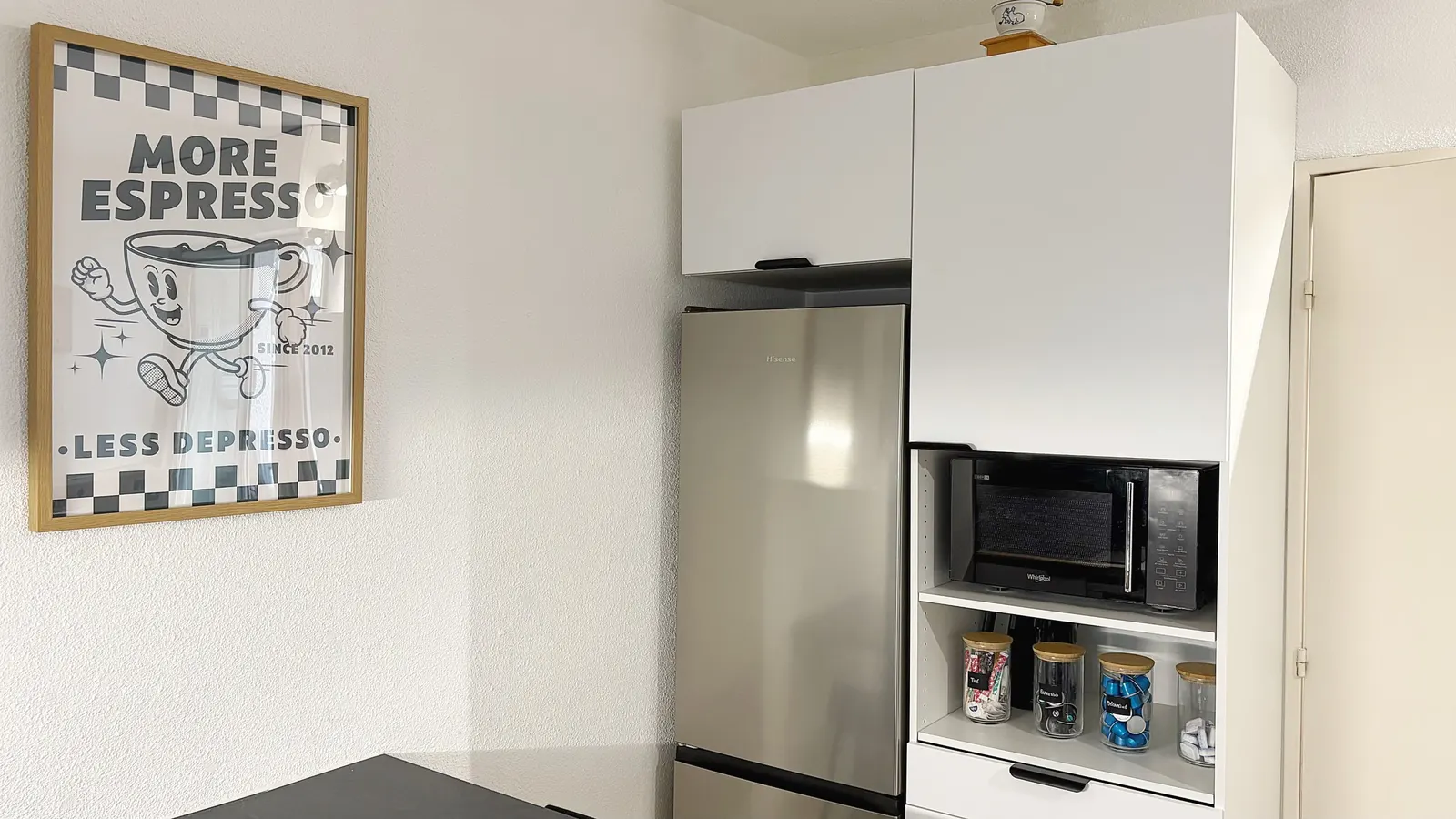 Cuisine vue en biais : réfrigérateur, micro-ondes et plan de travail